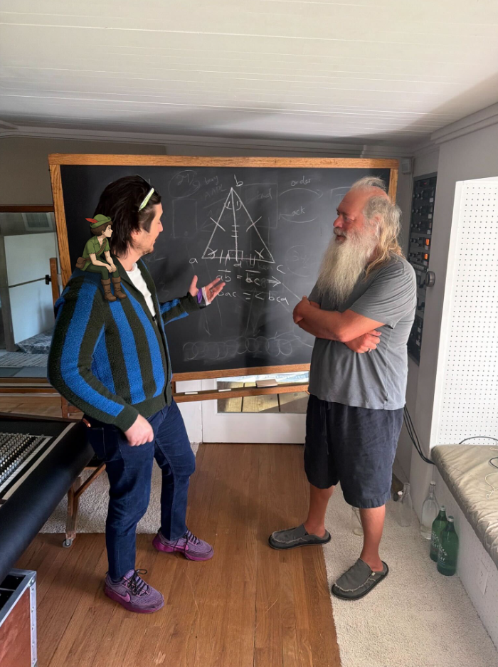 Community photo edit: tiny Little Guy sits on Vlad Tenev's shoulder as he talks beside a chalkboard.
